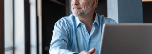Mature businessman working on laptop. Handsome mature business leader sitting in a modern office with large windows