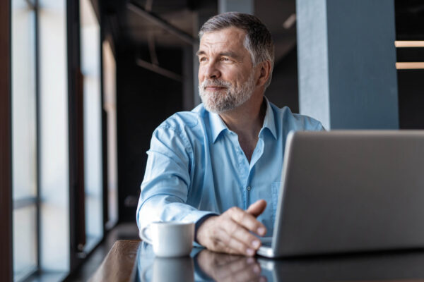 Mature businessman working on laptop. Handsome mature business leader sitting in a modern office with large windows