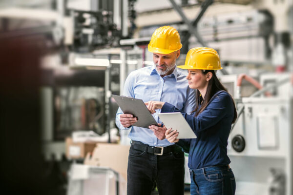 Two project managers standing in modern industrial factory. Manufacturing facility with robotics, robotic arms and automation. Storing products and materials in warehouse. Two project managers standing in modern industrial factory. Manufacturing facility with robotics, robotic arms and automation.