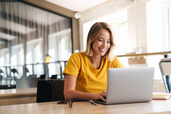 Frau-blond-in-gelben-Shirt-schaut-auf-Laptop