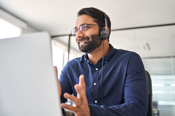 Happy-call-center-agent-wearing-headset-talking-to-client-working-in-customer-support-office.-Professional-contract-service-telemarketing-operator-using-laptop-having-conversation.